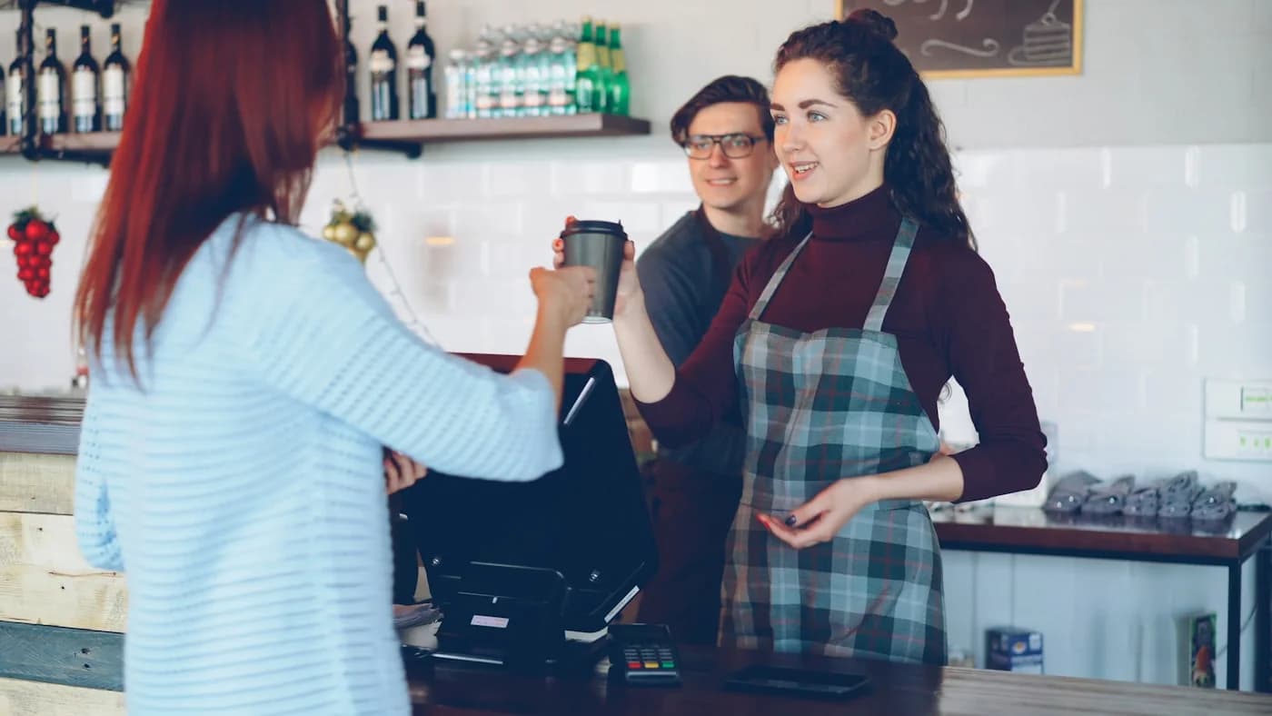 Una barista entrega un café a una clienta en la barra.